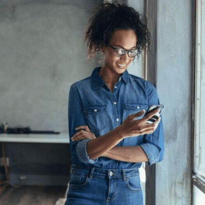 Woman on her phone by a window, representing Invisalign® Virtual Care AI