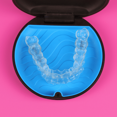 Invisalign aligners in a blue case on a pink background, representing orthodontic treatment