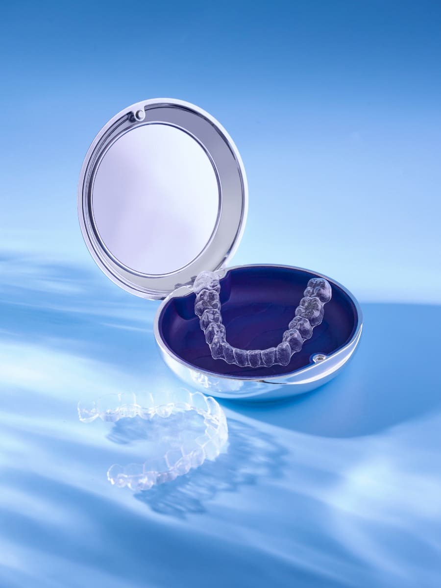 Clear Invisalign or Smile Express aligner trays displayed in a silver compact case on a blue background.