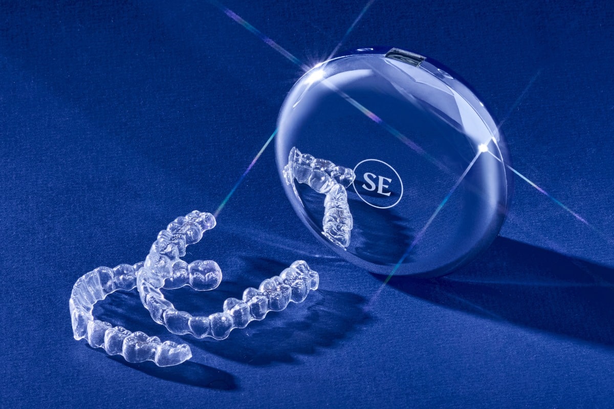 Clear Smile Express aligner trays with carrying case on blue background.